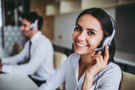 How can I help you? Beautiful call center workers in headphones are working at modern office.の写真素材