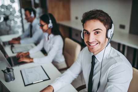 How can I help you? Beautiful call center workers in headphones are working at modern office.の写真素材