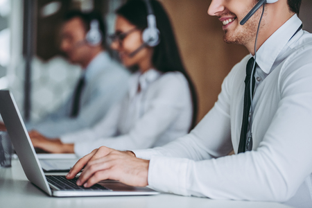 How can I help you? Beautiful call center workers in headphones are working at modern office.の写真素材