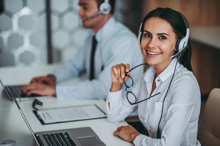 How can I help you? Beautiful call center workers in headphones are working at modern office.の写真素材