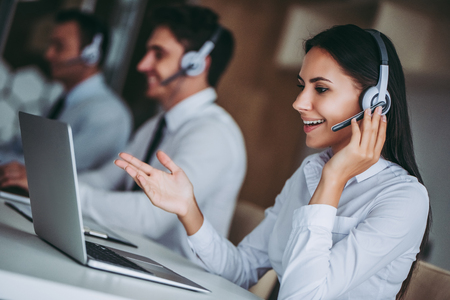 How can I help you? Beautiful call center workers in headphones are working at modern office.の写真素材