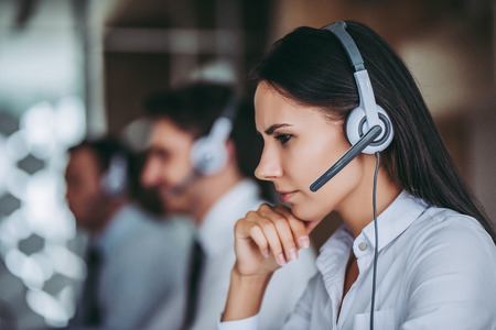 How can I help you? Beautiful call center workers in headphones are working at modern office.の写真素材