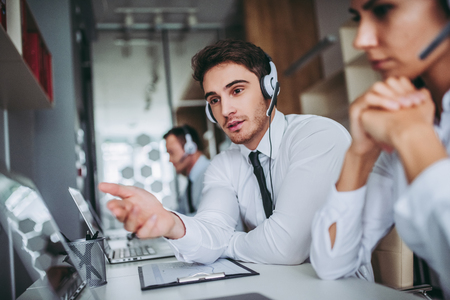 How can I help you? Beautiful call center workers in headphones are working at modern office.の写真素材