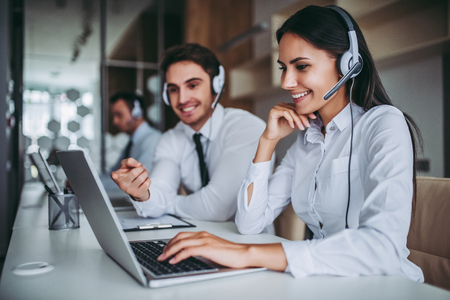How can I help you? Beautiful call center workers in headphones are working at modern office.の写真素材