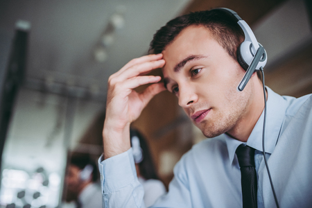 How can I help you? Beautiful call center workers in headphones are working at modern office. Feel of tirednessの写真素材