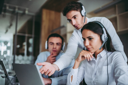 How can I help you? Beautiful call center workers in headphones are working at modern office.の写真素材