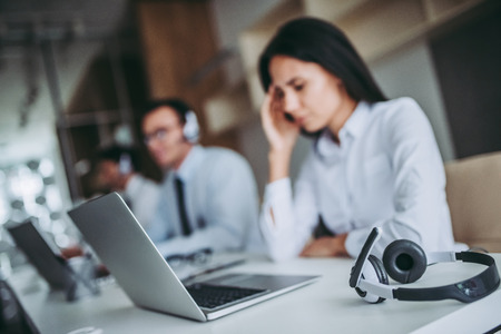 How can I help you? Beautiful call center workers are working at modern office. Feel of tiredness and headache.の写真素材