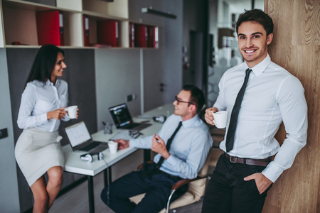 Beautiful young employees are taking coffee break. Workers in modern light office.の写真素材