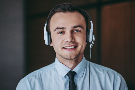 How can I help you?Portrait of handsome male call center worker in headphones smiling and looking at camera.の写真素材