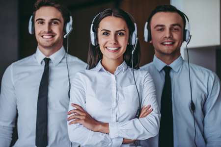 How can I help you? Portrait of beautiful call center workers in headphones are working at modern office, smiling and looking at camera.の写真素材