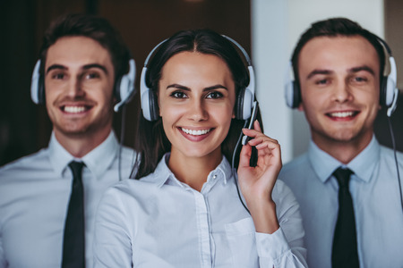 How can I help you? Portrait of beautiful call center workers in headphones are working at modern office, smiling and looking at camera.の写真素材