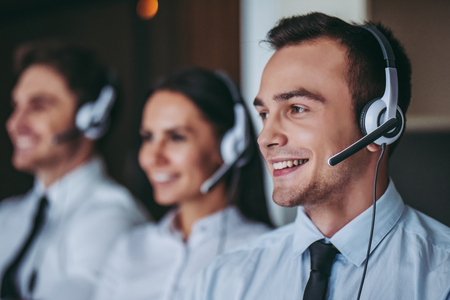 How can I help you? Portrait of beautiful call center workers in headphones are working at modern office.の写真素材