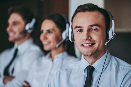 How can I help you? Portrait of beautiful call center workers in headphones are working at modern office, smiling and looking at camera.の写真素材