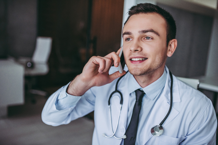 Young handsome doctor working. Talking on mobile phone and smiling.の写真素材
