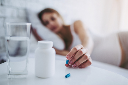 Attractive sick pregnant woman is lying in bed. Taking pills from colds. Last months of pregnancy.の写真素材