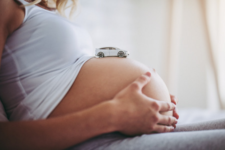 Cropped image of attractive pregnant woman is sitting in bed with toy car on belly. It's a boy Last months of pregnancy.の写真素材