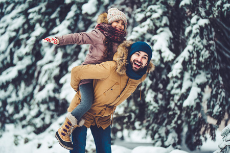 Handsome young dad and his little cute daughter are having fun outdoor in winter. Enjoying spending time together. Family concept.の写真素材
