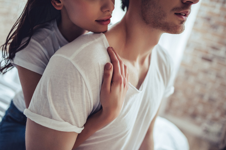 Cropped image of beautiful young couple is sitting on bed in bedroom. Enjoying spending time together at home.の写真素材