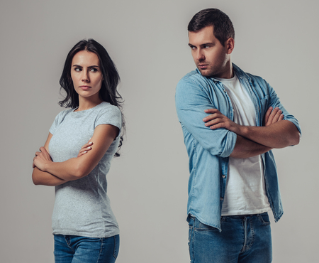 Beautiful romantic couple isolated on grey background. Standing apart from each other while being in a quarrel.