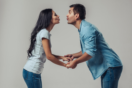 Beautiful romantic couple is standing on grey background, holding hands and going to kiss each other.の写真素材