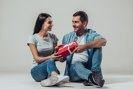 Beautiful romantic couple is sitting on grey background with gift box in hands.の写真素材