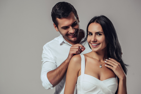 Beautiful romantic couple in love isolated on grey background. Handsome man is wearing necklace on his attractive young woman. Happy Saint Valentine's Day!の写真素材