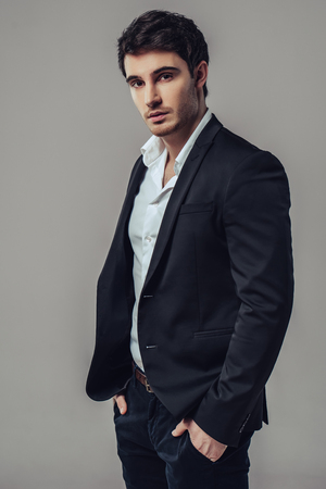 Handsome yound man in suit is posing on grey background.の写真素材