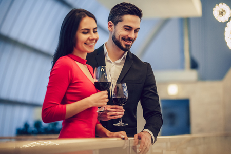 Beautiful loving couple is spending time together in modern restaurant. Attractive young woman in dress and handsome man in suit are having romantic dinner. Celebrating Saint Valentine's Day.の写真素材