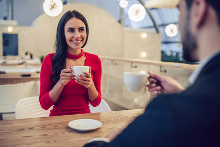 Beautiful loving couple is spending time together in modern restaurant. Attractive young woman in dress and handsome man in suit are having romantic dinner. Celebrating Saint Valentine's Day.の写真素材