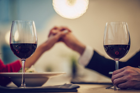 Cropped image of loving couple is spending time together in modern restaurant. Attractive young woman in dress and handsome man in suit are having romantic dinner. Celebrating Saint Valentine's Day.の写真素材