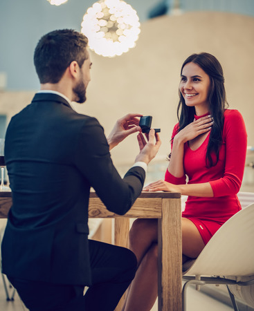 Beautiful loving couple is spending time together in modern restaurant. Attractive young woman in dress and handsome man in suit are having romantic dinner. Celebrating Saint Valentine's Day.の写真素材