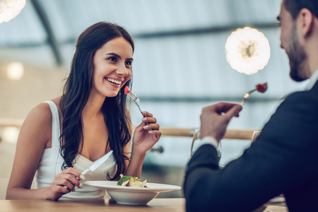 Beautiful loving couple is spending time together in modern restaurant. Attractive young woman in dress and handsome man in suit are having romantic dinner. Celebrating Saint Valentine's Day.の写真素材