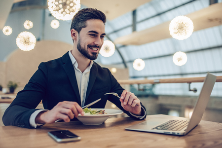 Handsome businessman is sitting in modern restaurant and working with laptopの写真素材