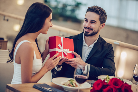 Beautiful loving couple is spending time together in modern restaurant. Attractive young woman in dress and handsome man in suit are having romantic dinner. Celebrating Saint Valentine's Day.の写真素材