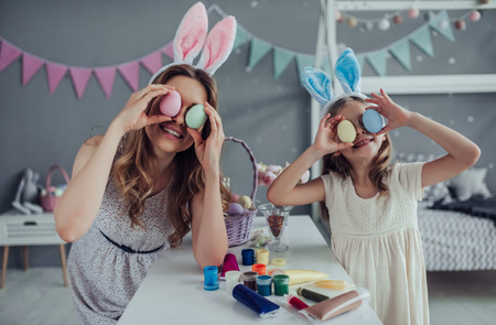 Attractive young woman with little cute girl are preparing for Easter celebration. Mom and daughter wearing bunny ears are spending time together before Easter while painting eggs.の写真素材