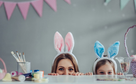 Attractive young woman with little cute girl are preparing for Easter celebration. Mom and daughter wearing bunny ears are spending time together before Easter.の写真素材