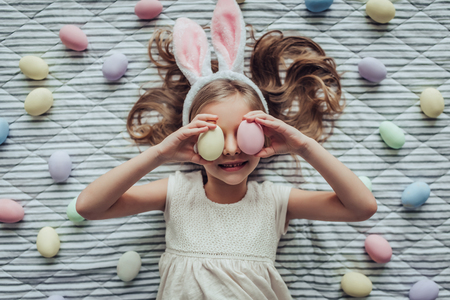 Little cute girl is preparing for Easter celebration. Lying on the floor with many colorful Easter eggs nearby.の写真素材
