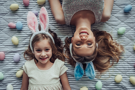 Attractive young woman with little cute girl are preparing for Easter celebration. Mom and daughter wearing bunny ears are lying on the floor full of painted Easter eggs.の写真素材