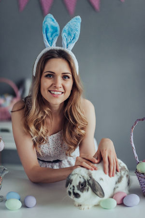 Attrective young woman wearing bunny ears is preparing for Easter celebration while having fun with Easter bunny at home.の写真素材