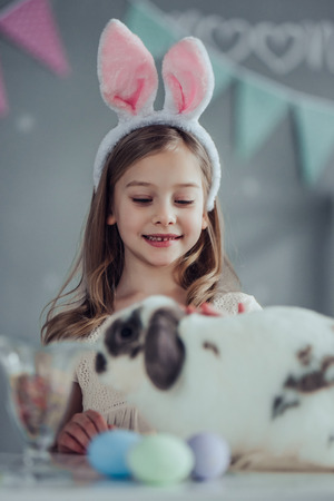Little girl with bunny ears is preparing for Easter celebration while having fun with cute bunny.の写真素材