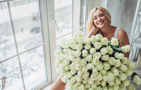 Attractive young woman with bouquet of hundreds of white roses is spending time at home.の写真素材