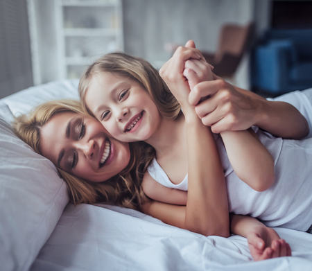 Attractive young woman with little cute girl are spending time together at home. Lying on bed, hugging and having fun. Happy family concept. Mother's day.の写真素材