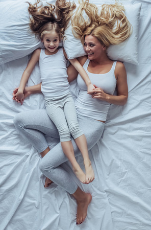 Top view image of attractive young woman with little cute girl are spending time together at home. Lying on bed, hugging and having fun. Happy family concept. Mother's day.の写真素材