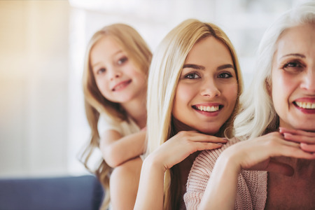 Little cute girl, her attractive young mother and charming grandmother are spending time together at home. Women's generation. Happy International Women's Day!の写真素材
