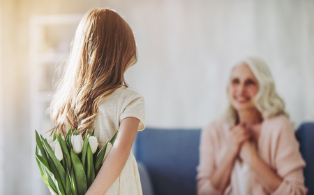 Little cute girl is presenting flowers to her grandmother while spending time together at home. Happy Women's Day!の写真素材
