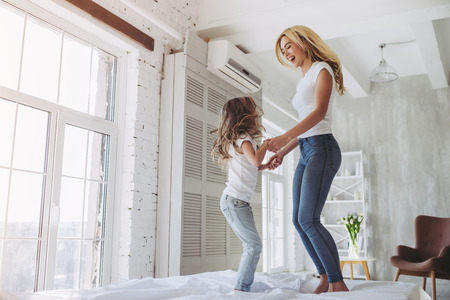 Attractive young woman and her little cute daughter are having fun in bed while being at home together. Happy Mother's Day!の写真素材