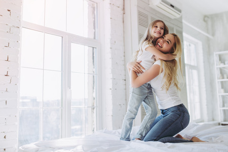 Attractive young woman and her little cute daughter are having fun in bed while being at home together. Happy Mother's Day!の写真素材