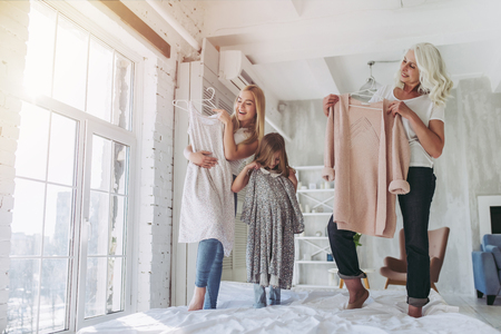 Little cute girl, her attractive young mother and charming grandmother are fitting clothes while spending time together at home. Women's generation. International Women's Day. Happy Mother's Day.の写真素材