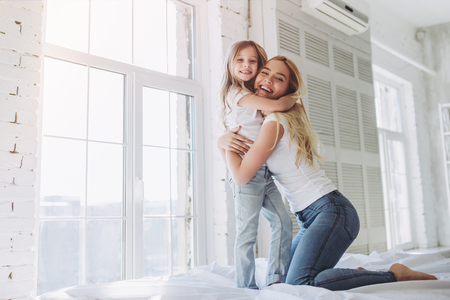 Attractive young woman and her little cute daughter are having fun in bed while being at home together. Happy Mother's Day!の写真素材