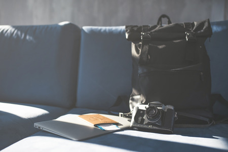 Pasport, tickets, camera and travel bag are lying on sofa in light room. Preparing for travelingの写真素材